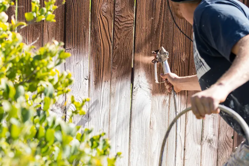Professional fence painter painting a fence with a spray nozzle